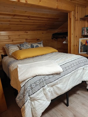 A wooden cabin bedroom with a bed, pillows, and a shelf with books. - Lake House on Bluff Lake - Nature Lovers Paradise (Lake)