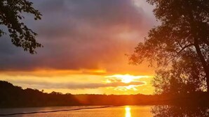 Une vue sur le coucher de soleil au-dessus d’un lac paisible, avec un quai et des arbres.