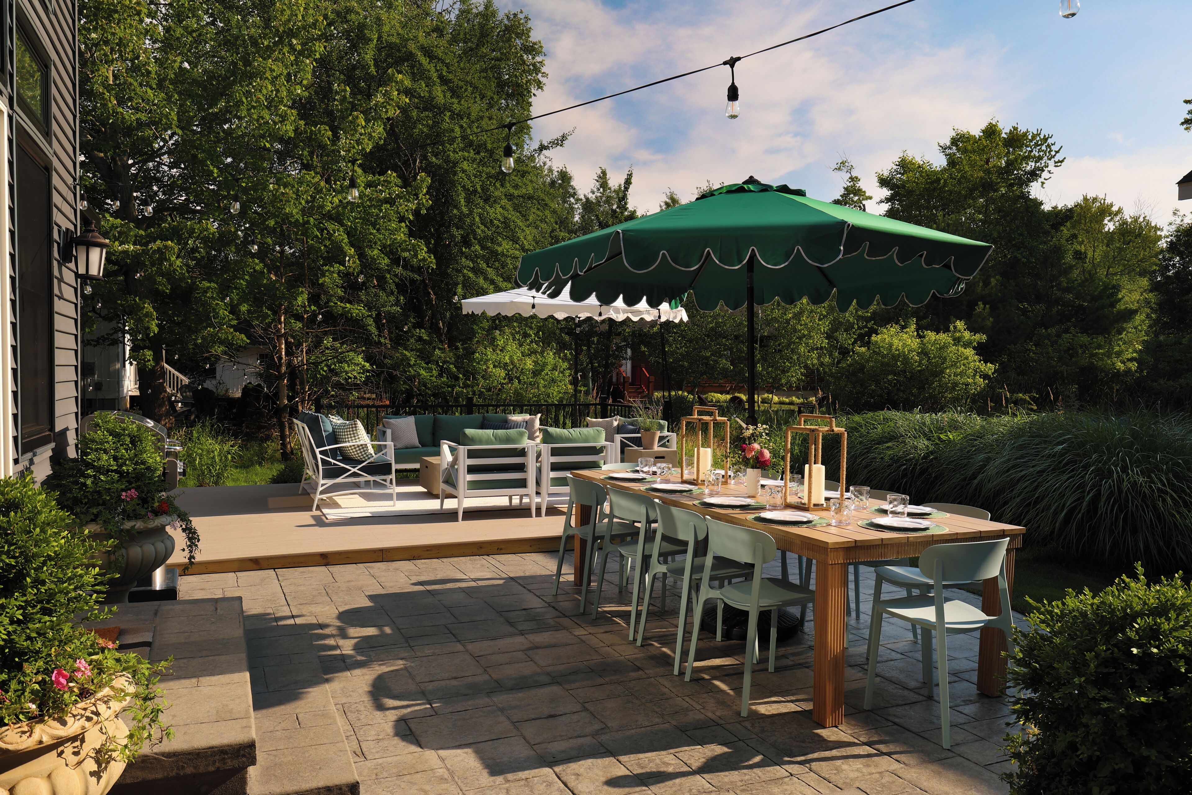 En udendørs terrasse med spisebord, stole og en grøn parasol.