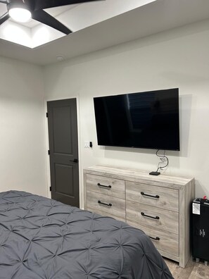 Een slaapkamer met een bed, een dressoir, een televisie en een plafondventilator.