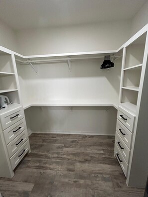 Un dressing accessible sans porte, doté d’étagères ouvertes, d’une tringle et d’un porte-chaussures.