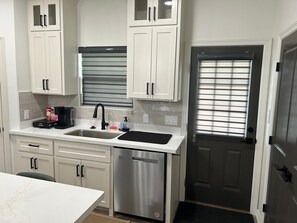 A kitchen with white cabinets, a stainless steel dishwasher, a black faucet, and a window with blinds. - Comfortable & Cozy Home Donna, TX (Donna)