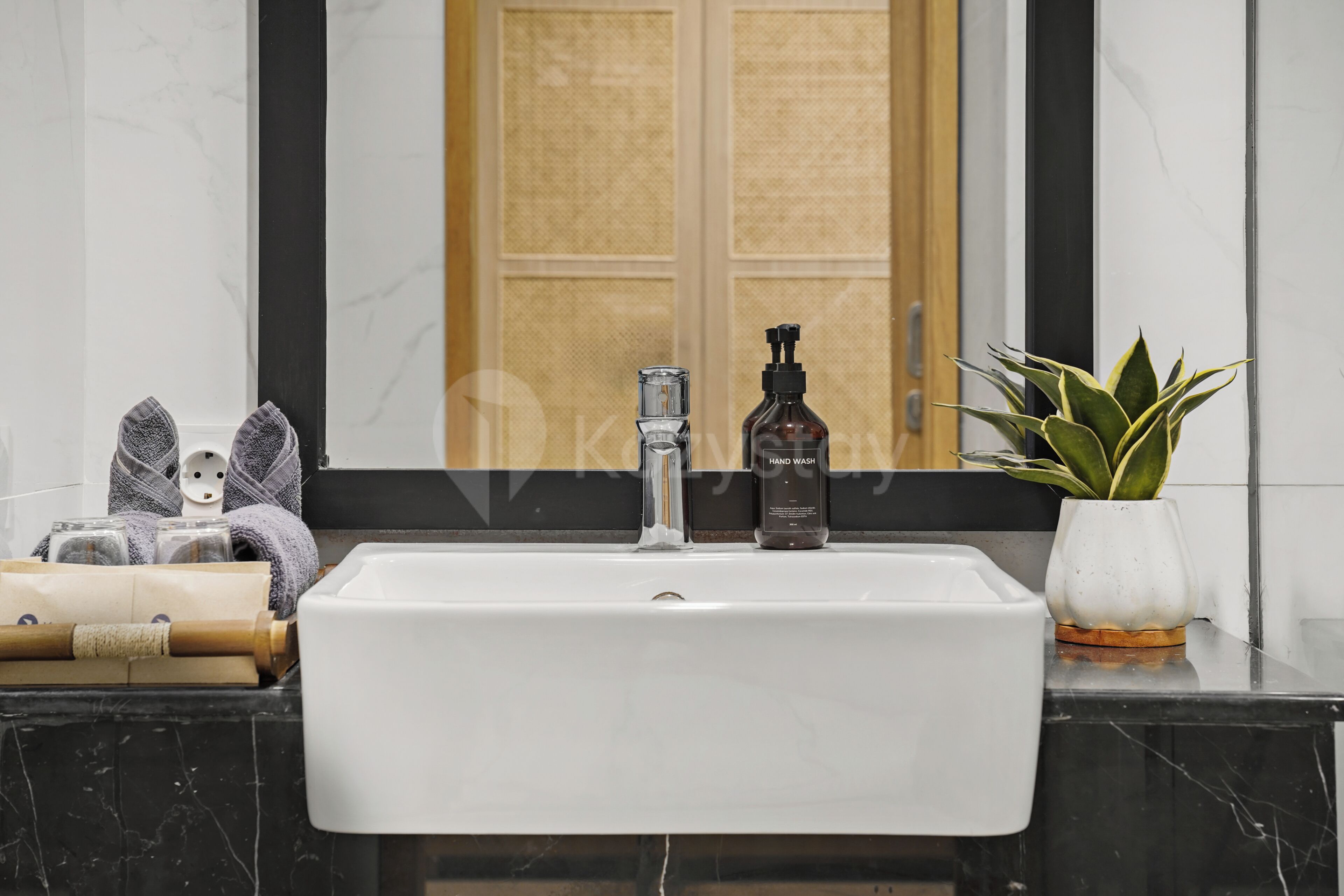 A bathroom with a white sink, a mirror, a wooden door, and a potted plant.