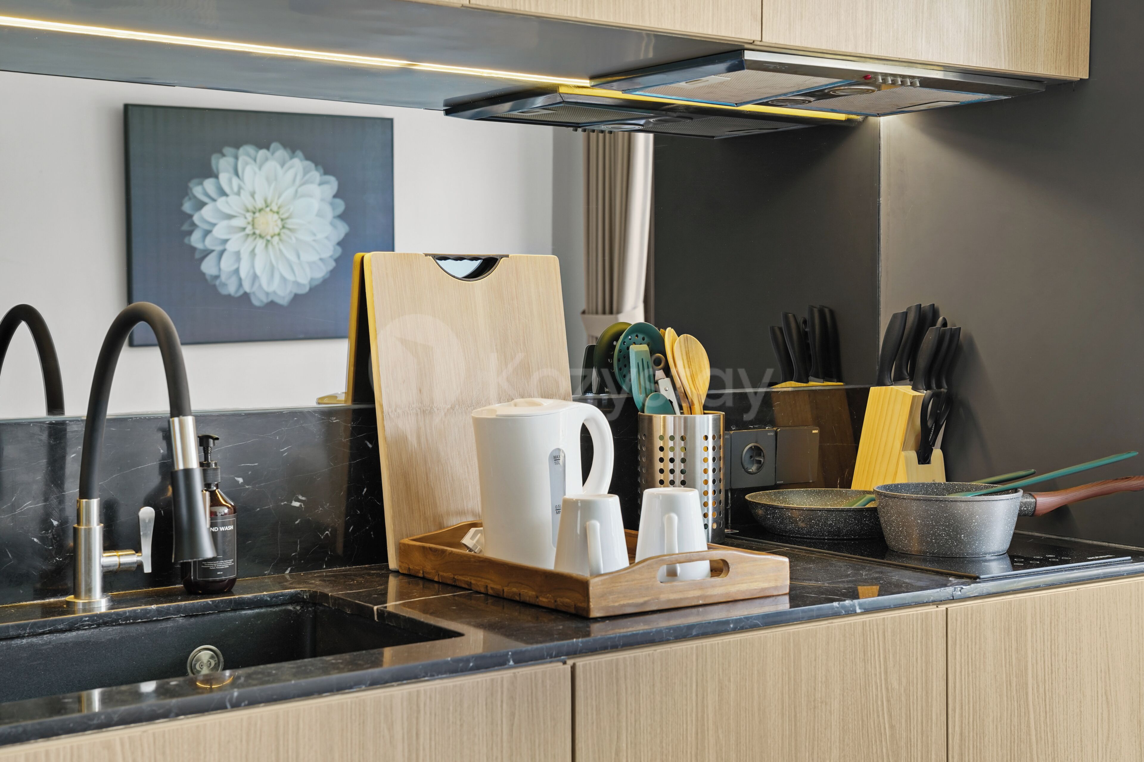 Een moderne keuken met een zwart aanrecht, roestvrijstalen apparatuur en een houten snijplank met bestek.