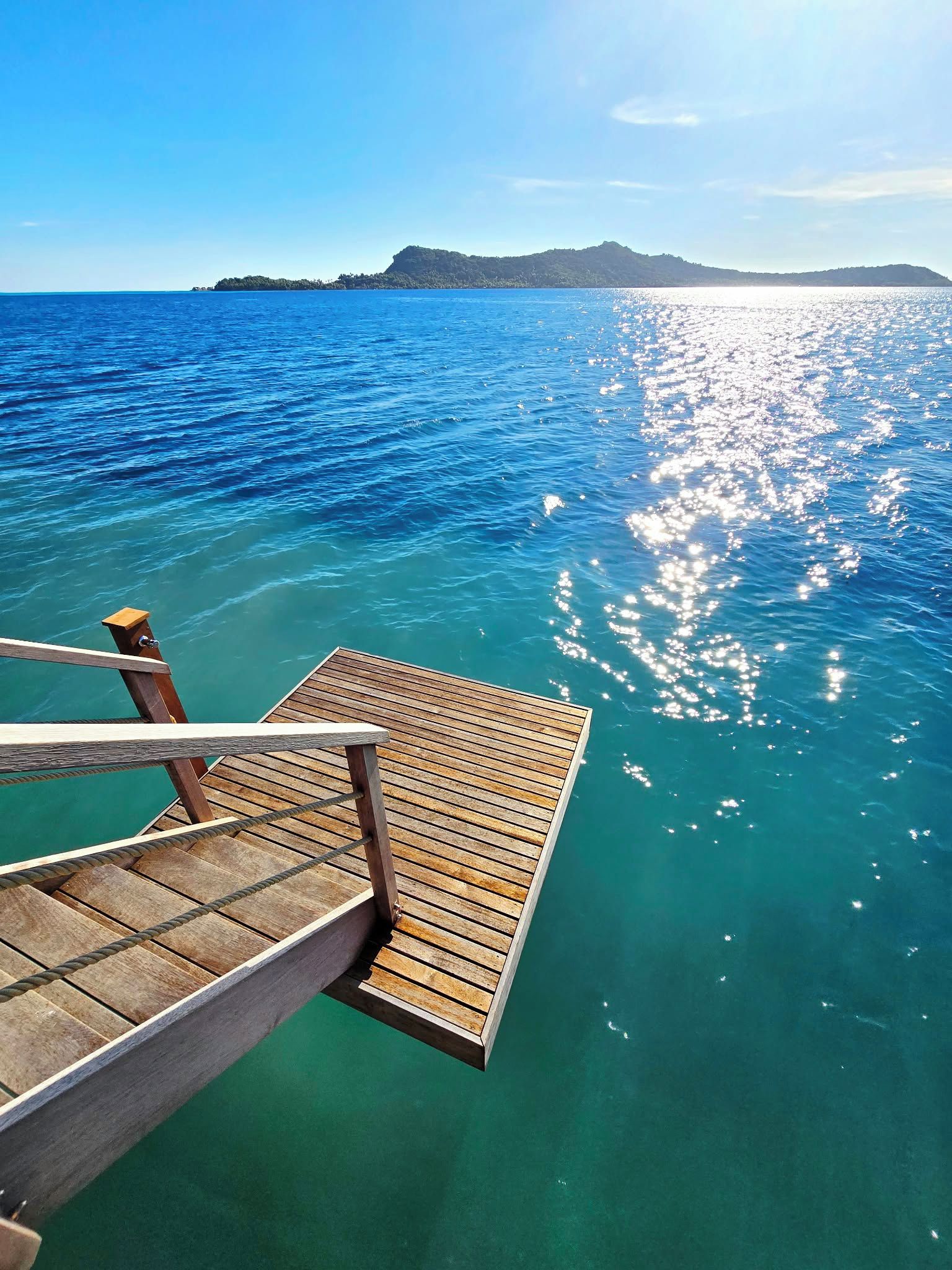 A wooden deck extending into clear turquoise water with a distant landmass.