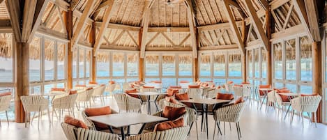 A spacious indoor area with high ceilings, large windows, and a view of the sea.