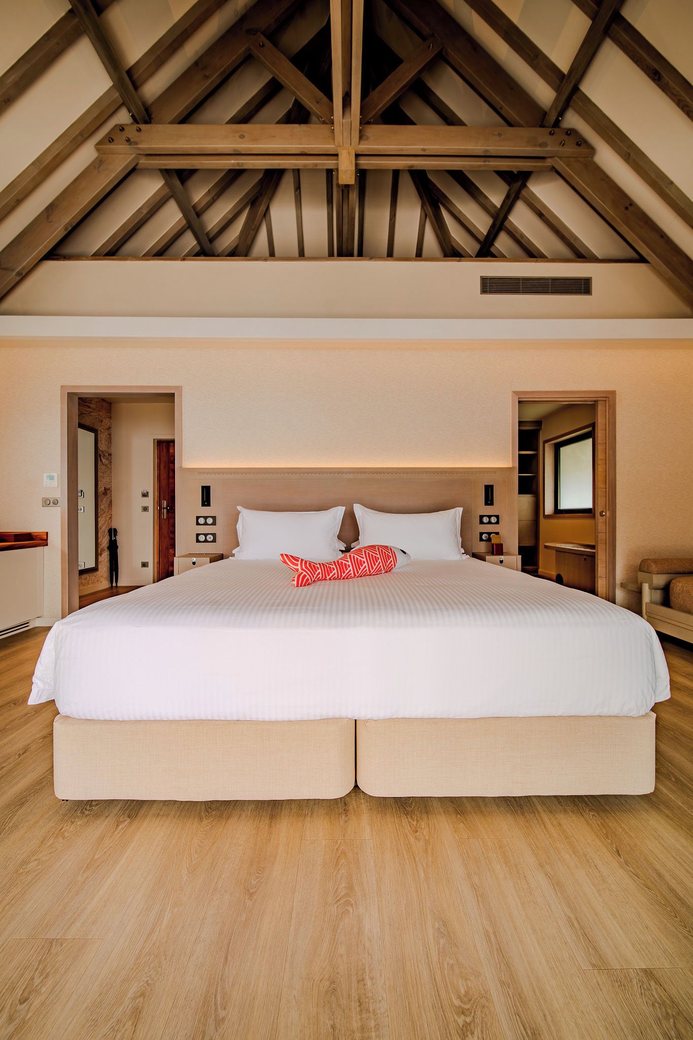 Una cama grande con cabecera, suelo de madera y techo abovedado.