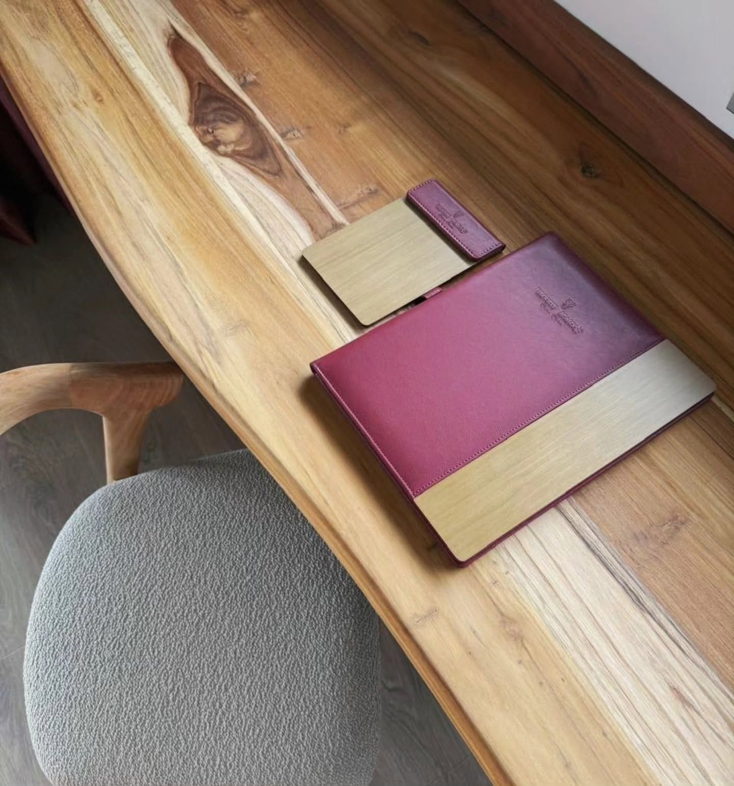 A wooden desk with a notebook, a pen, and a small notebook on it.