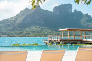 A poolside view with lounge chairs, a wooden deck, and a mountain backdrop. - Bloody Mary's Hotel (Bora Bora)