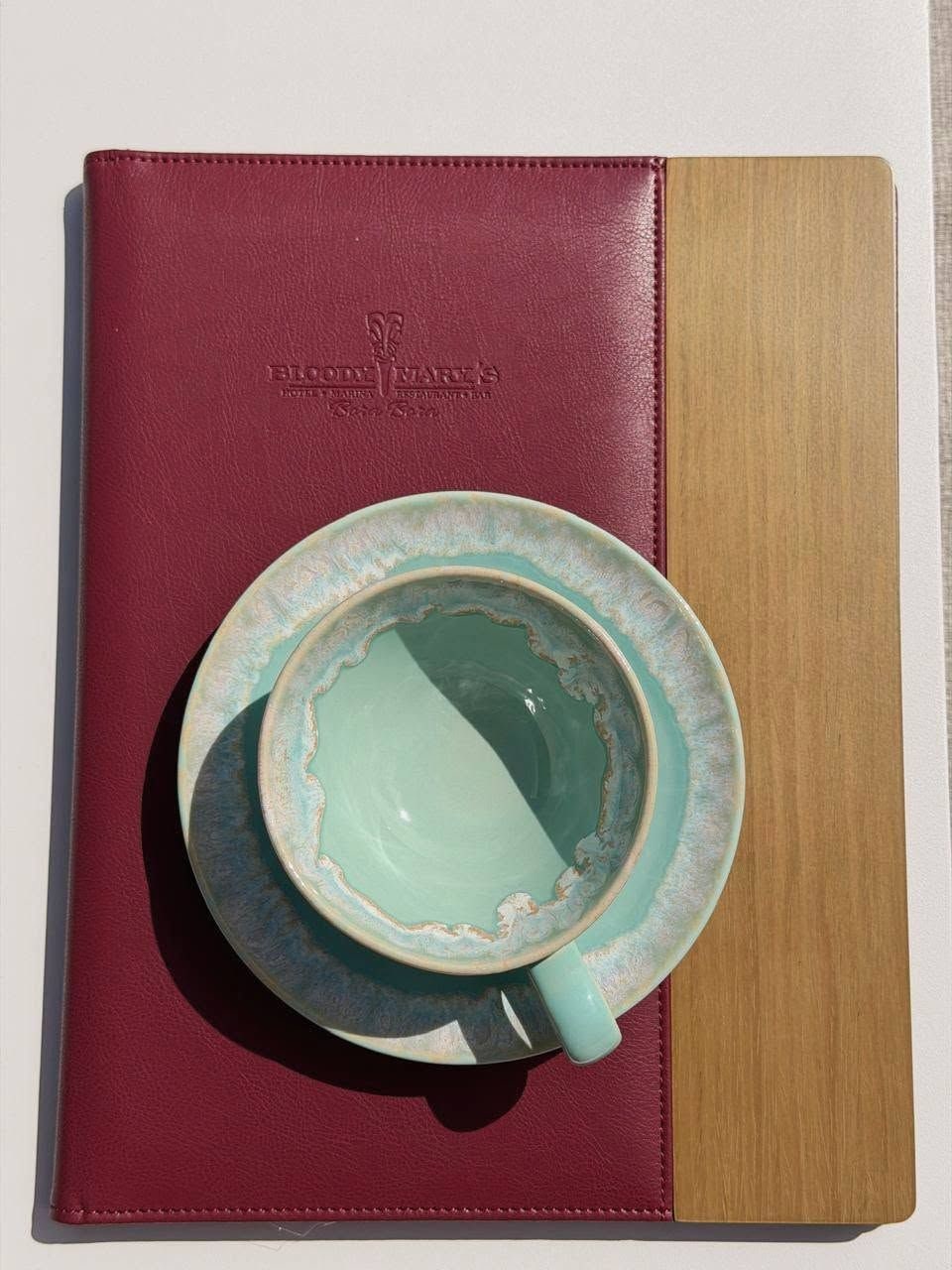 Un cuaderno de cuero rojo con tapa de madera, una taza de cerámica turquesa y un platillo a juego.