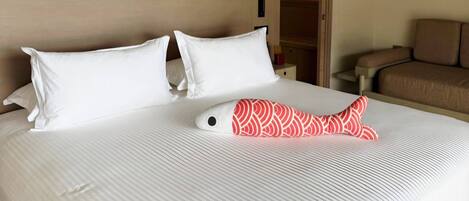 Une chambre d’hôtel avec un lit, des oreillers blancs, un coussin à motifs rouges et blancs, une table de chevet et un canapé marron.