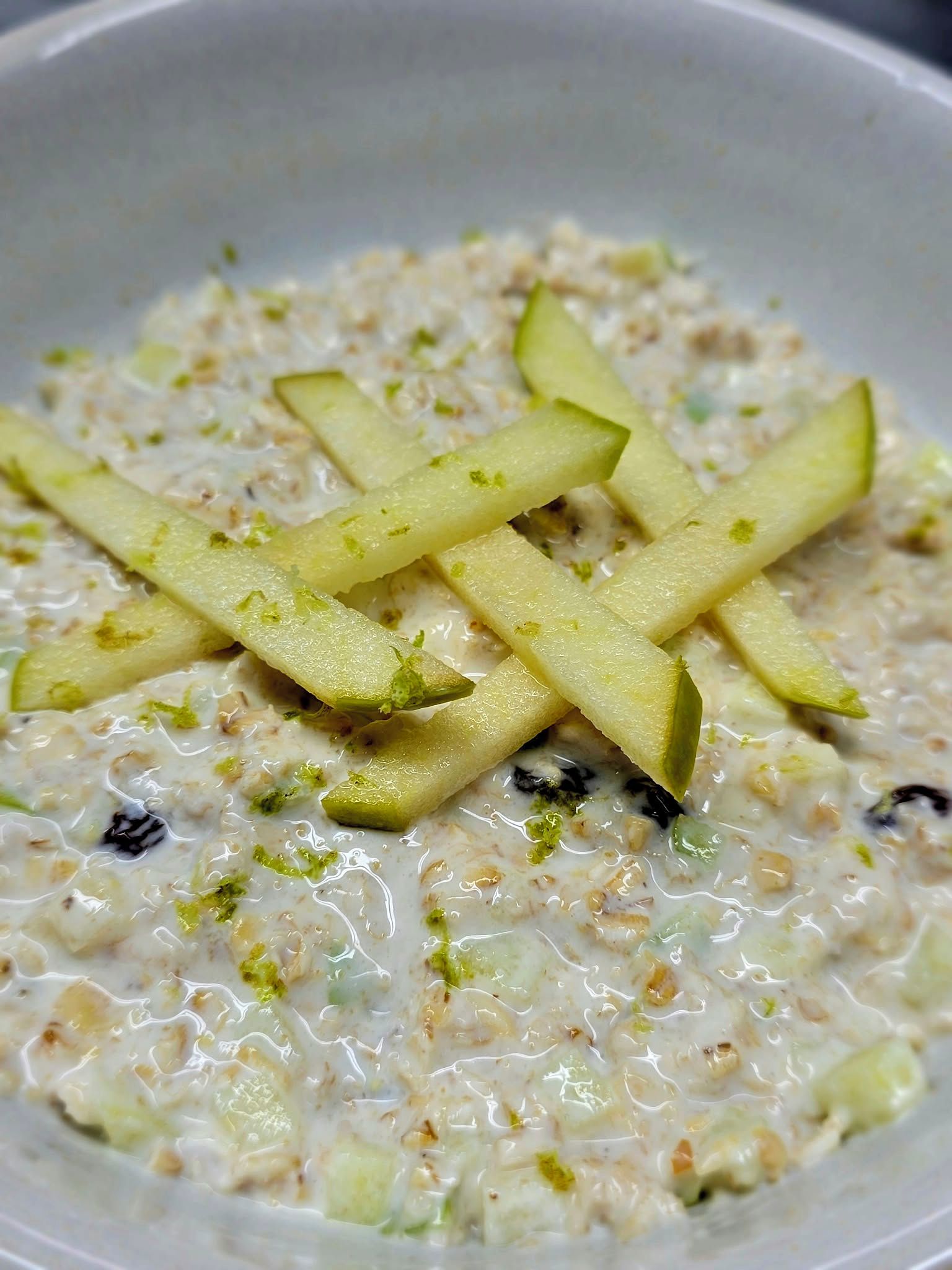 A bowl of oatmeal with apple slices and raisins.