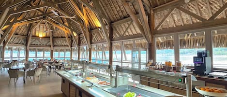 A buffet area with a high ceiling and natural light, featuring a variety of food options and seating arrangements.