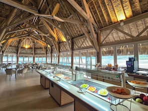 A buffet area with a high ceiling and natural light, featuring a variety of food options and seating arrangements.