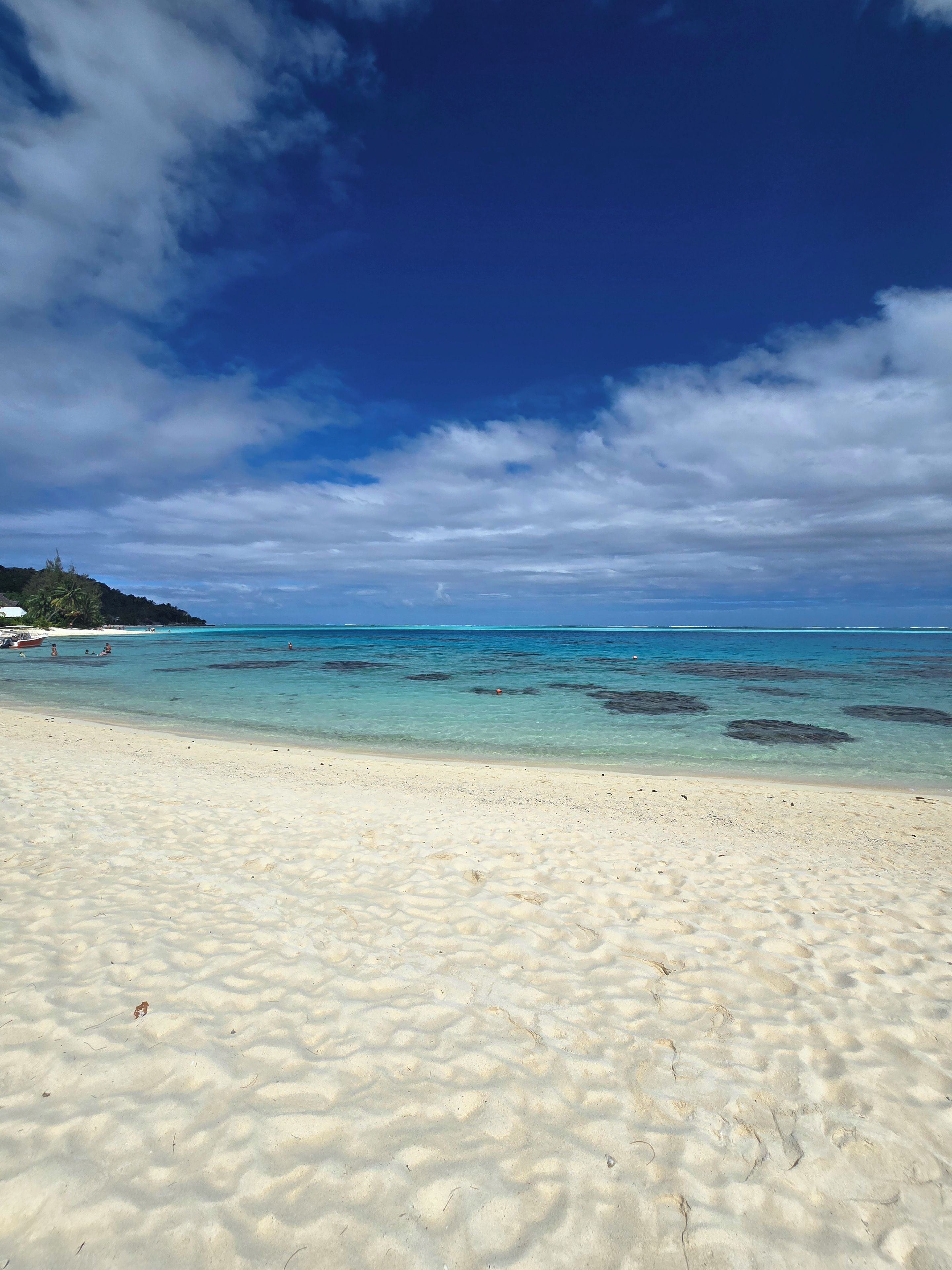 Una playa con agua turquesa cristalina, arena blanca y una colina distante con vegetación.