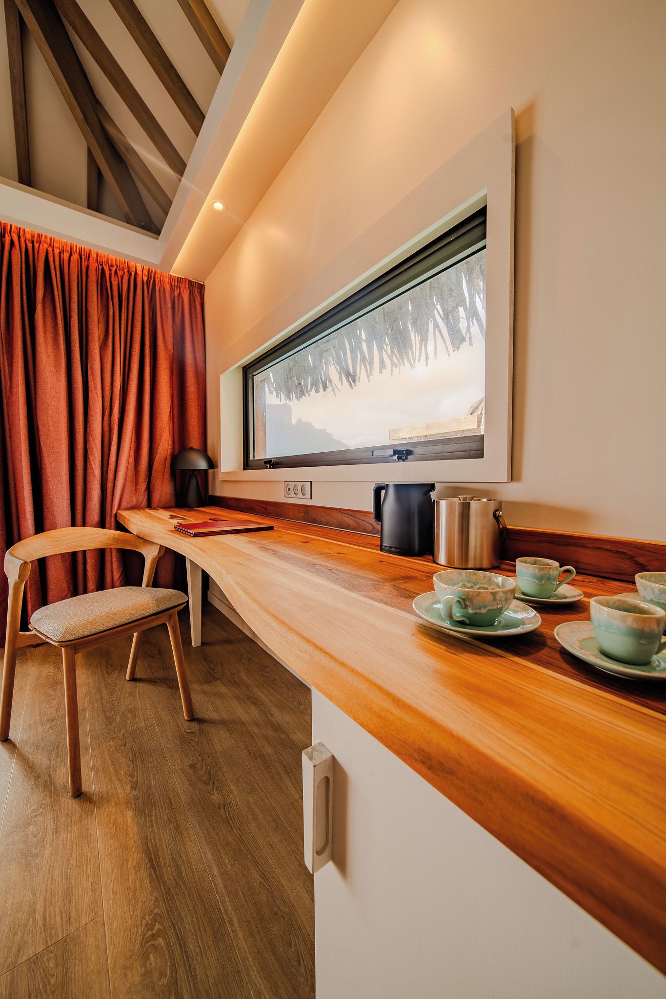 A cozy kitchen with a wooden countertop, a window with a view of trees, and a kettle.