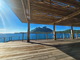 Una terraza de madera con vista al mar y una montaña al fondo.