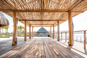 Una terraza de madera con estructura de techo de paja que conduce a un edificio con techo de paja.