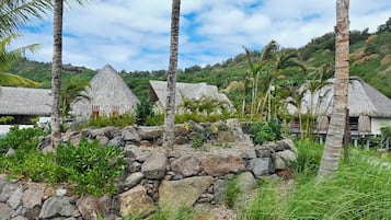 A tropical resort with thatched-roof huts, palm trees, and a stone wall.