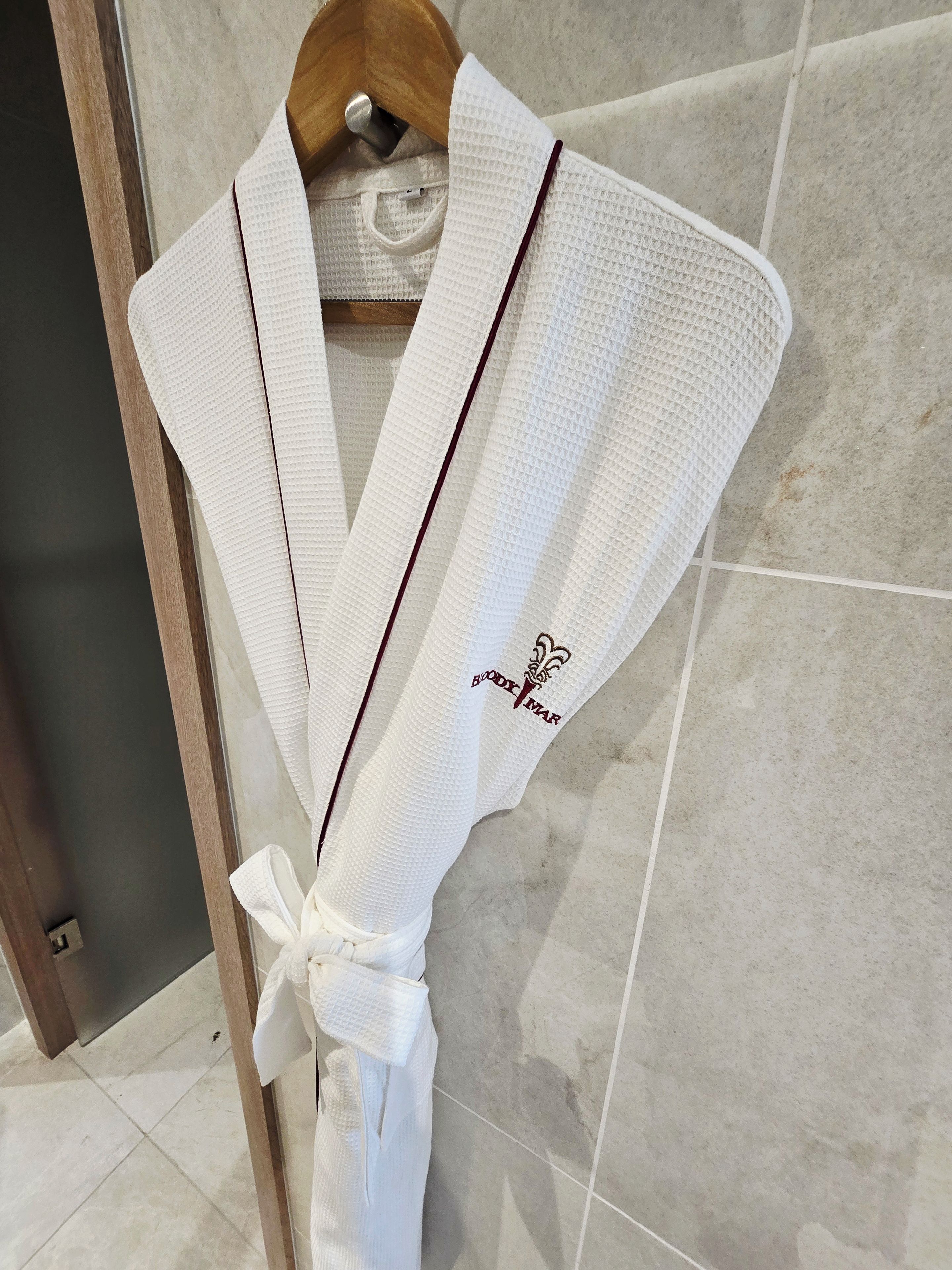 A white robe with a bow and a logo on the sleeve, hanging on a wooden hanger.