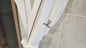 A white robe with a bow and a logo on the sleeve, hanging on a wooden hanger.