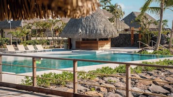 Ein Poolbereich mit Liegestühlen, einer strohgedeckten Struktur und tropischer Bepflanzung.