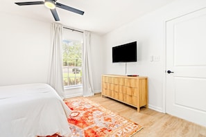 Un dormitorio con cama, televisor montado en la pared, un armario de madera y una ventana con cortinas.