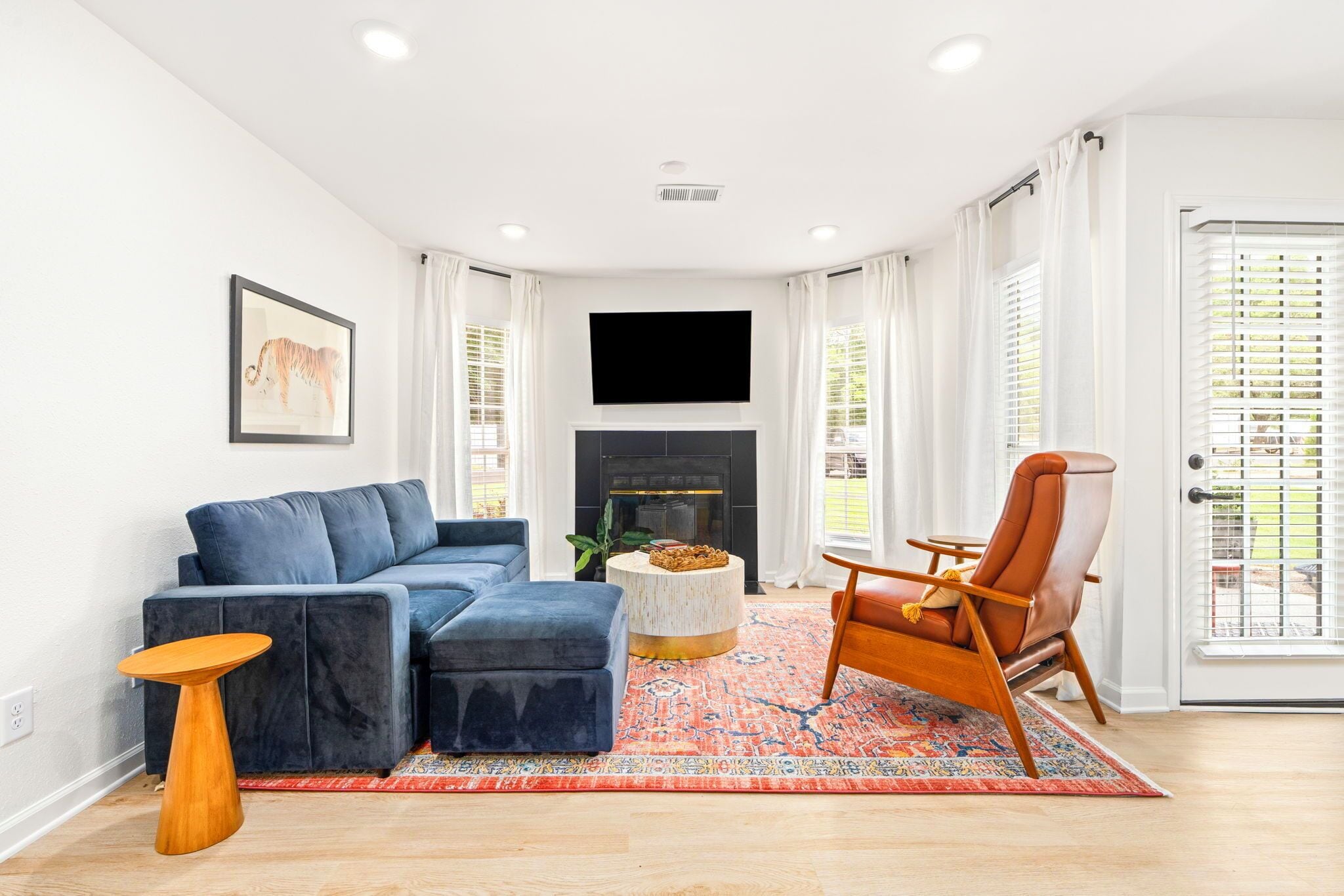 A living room with a blue sofa, a wooden coffee table, a patterned rug, a brown leather chair, and a fireplace.