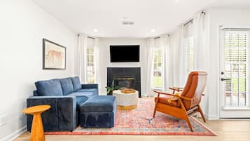 A living room with a blue sofa, a wooden coffee table, a patterned rug, a brown leather chair, and a fireplace.