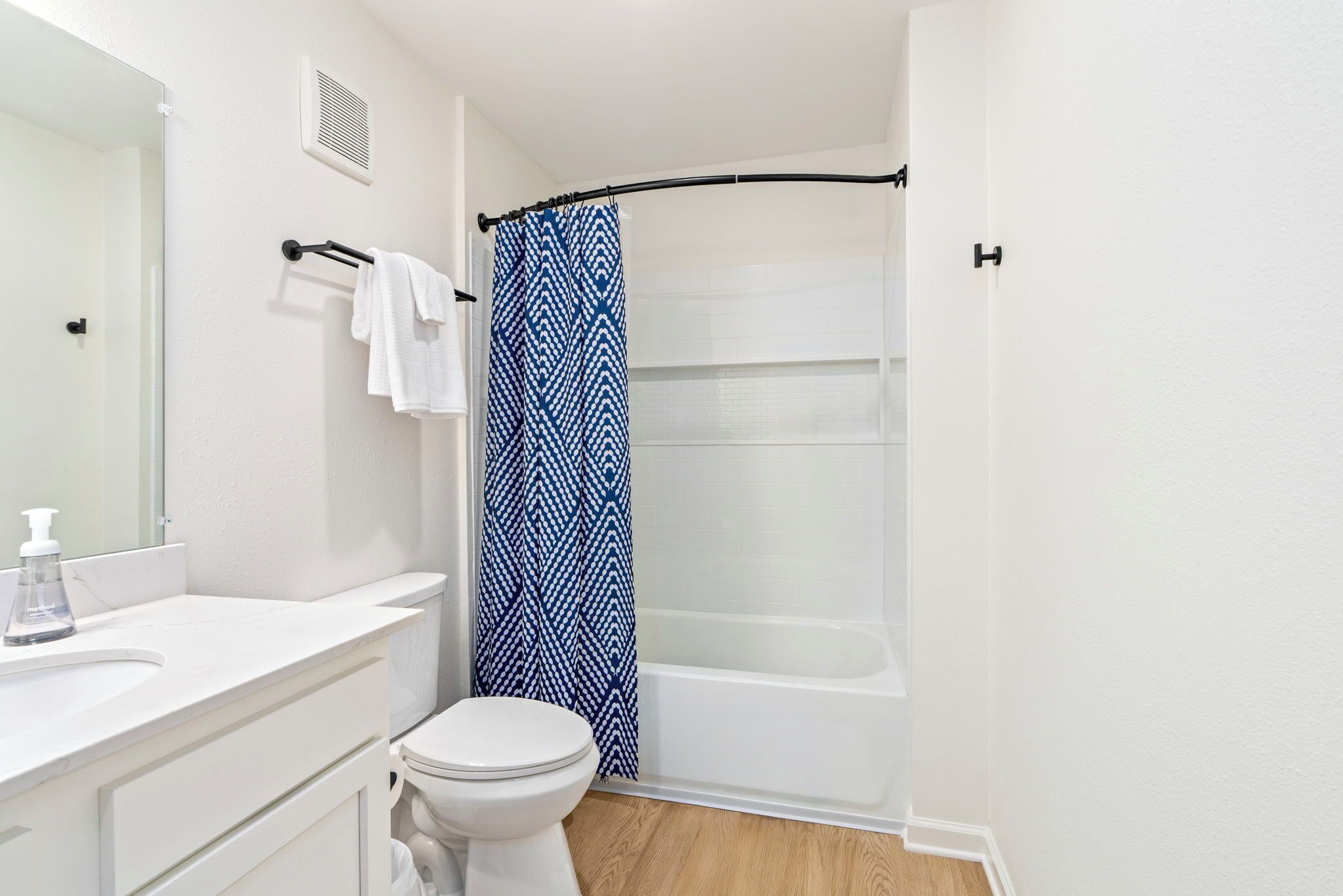 Un baño con inodoro y lavamanos blancos, y una cortina de ducha con diseño azul.