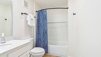 Un baño con inodoro y lavamanos blancos, y una cortina de ducha con diseño azul.