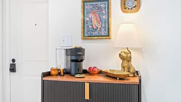Et tekøkken med kaffemaskine, en skål med frugt og en dekorativ lampe.