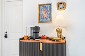 Una kitchenette con una cafetera, un frutero y una lámpara decorativa.