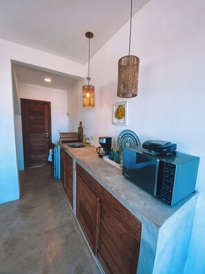 A kitchen with wooden cabinets, a microwave, a coffee maker, and hanging pendant lights. - Wake up to the sea | 3 suites | Monte Alto Beach (Arraial do Cabo)