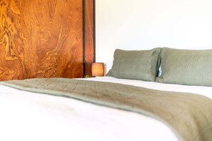 Un lit avec une couverture matelassée et deux oreillers, une tête de lit en bois et une lampe de chevet.