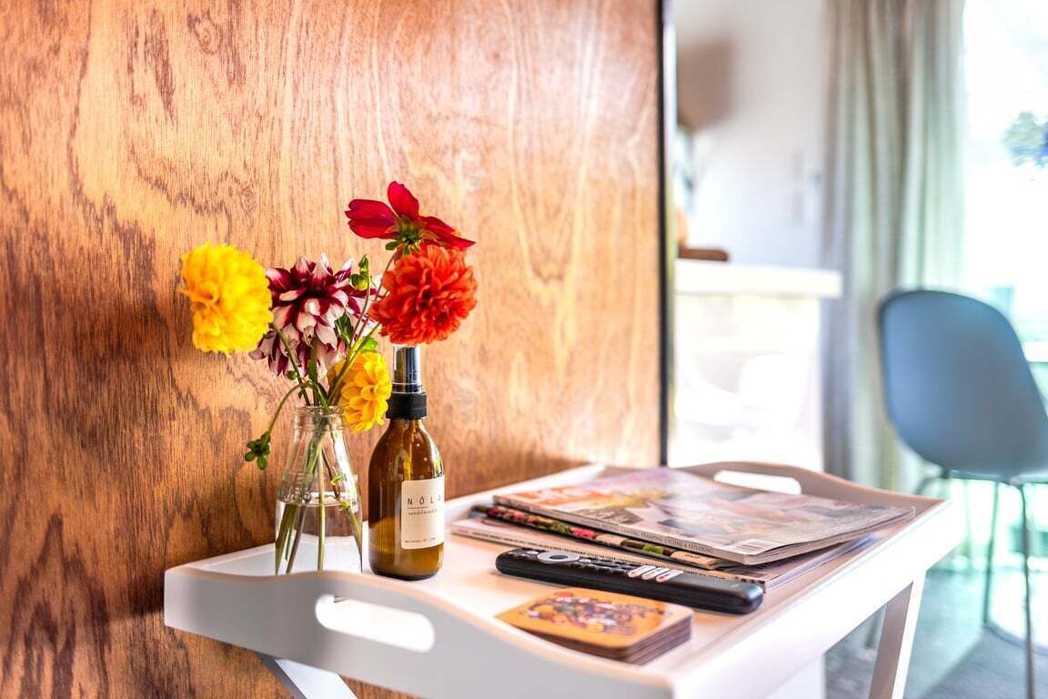 Un plateau blanc avec une bouteille, un vase rempli de fleurs et des magazines sur une table.