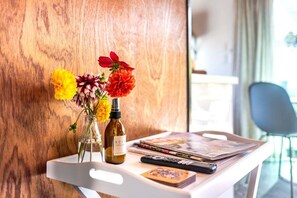 Un plateau blanc avec une bouteille, un vase rempli de fleurs et des magazines sur une table.