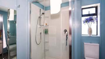 A bathroom with a glass-enclosed shower, a toilet, and a window with a vase of flowers.