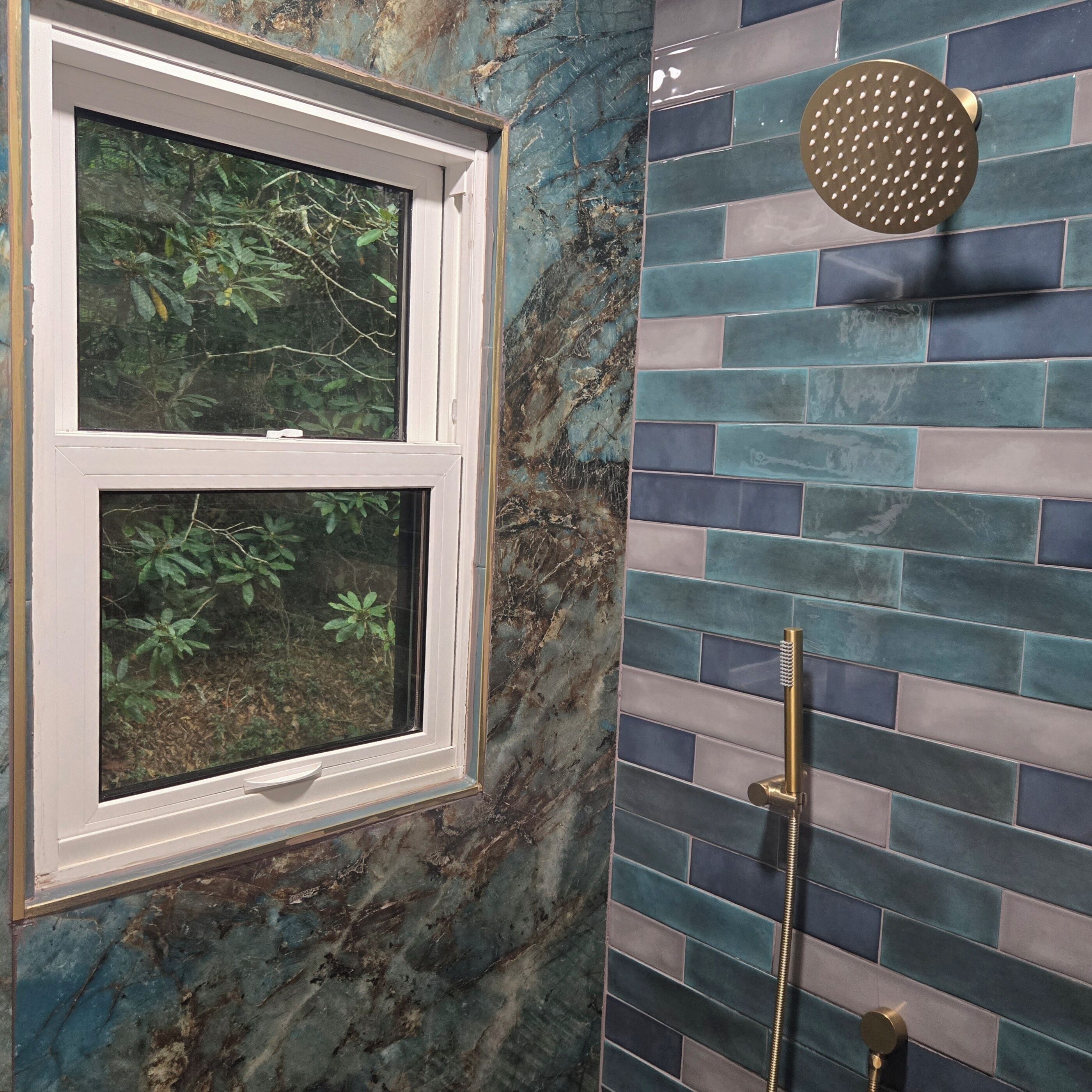A bathroom with a window, a shower with a gold showerhead, and a tiled wall.