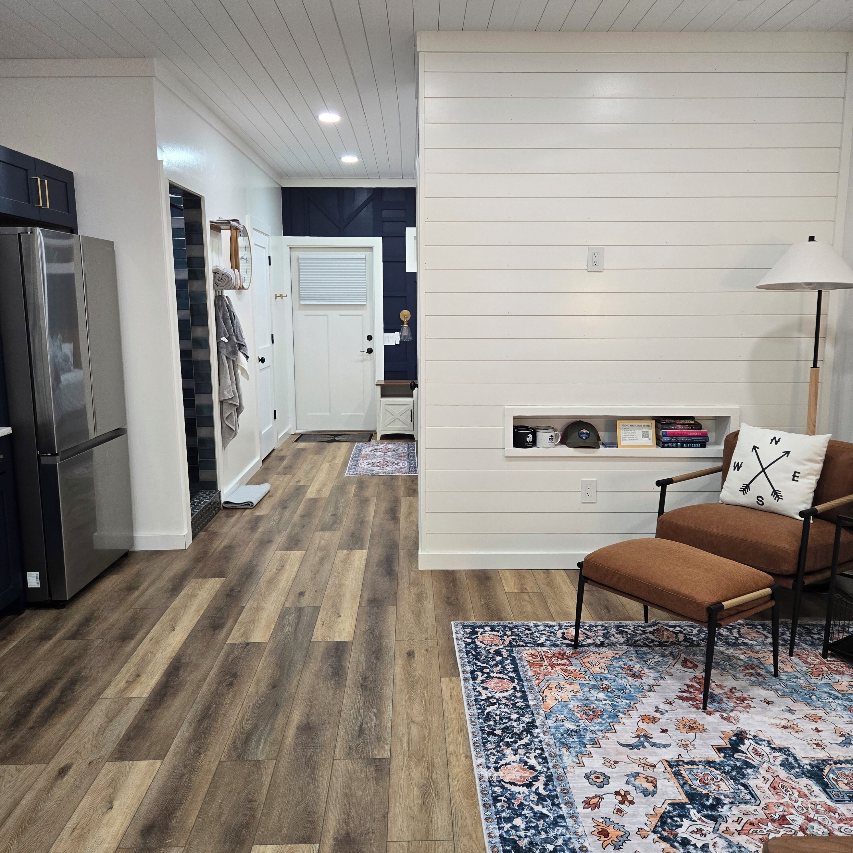 A modern kitchen with a refrigerator, wooden flooring, and a white wall with a built-in shelf.