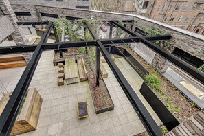 Une terrasse sur le toit, dotée d’une structure métallique, de jardinières en bois et offrant une vue sur les bâtiments environnants.