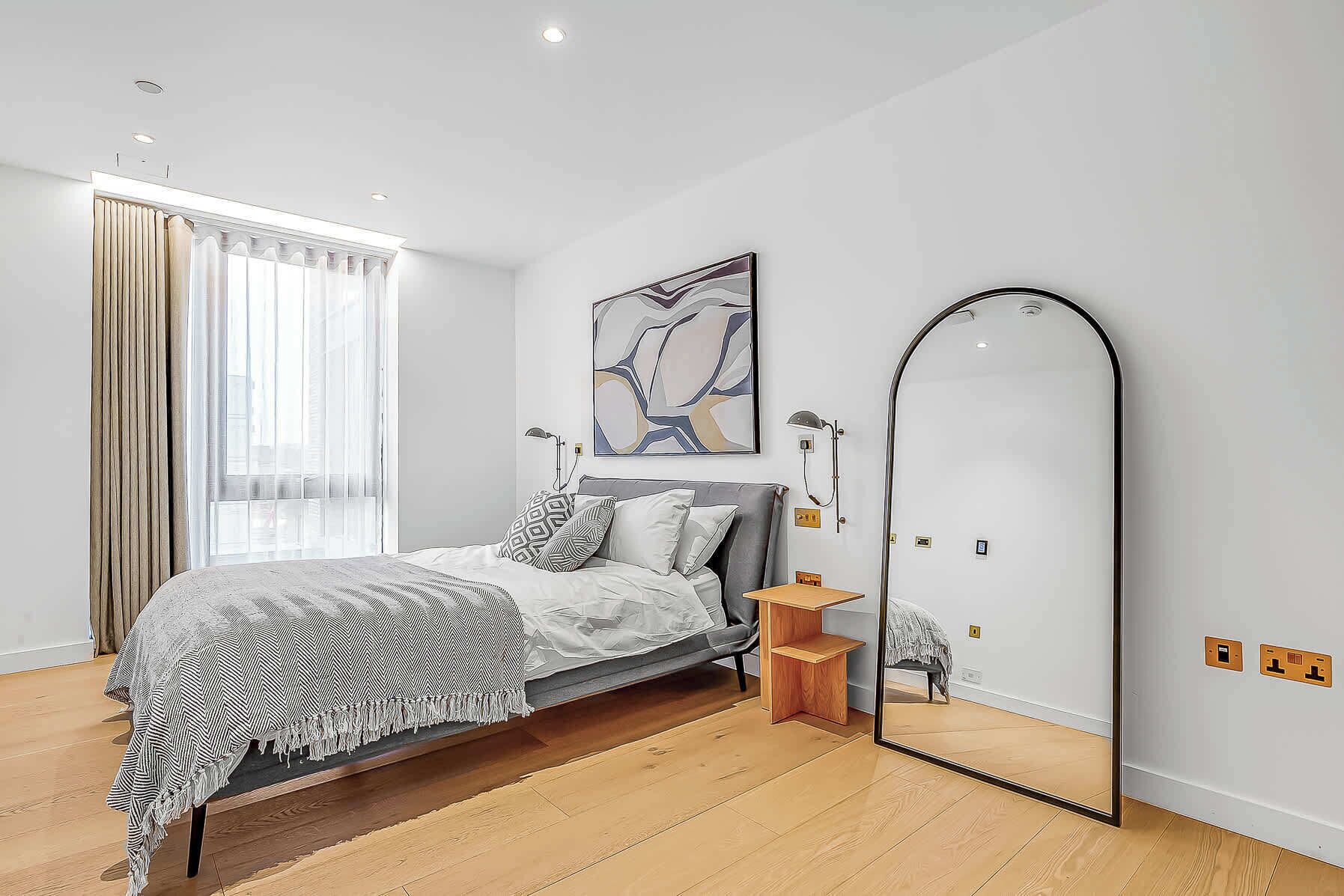 Un dormitorio moderno con cama, un espejo grande y una ventana con cortinas.