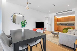 A modern living space with a dining area, a television, a kitchen, and a seating area. - AC | Private Balcony | Gym  | StayCozy (London)