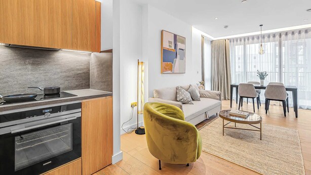 A modern kitchen with a built-in oven and a dining area with a sofa and chairs. - AC | Private Balcony | Gym  | StayCozy (London)