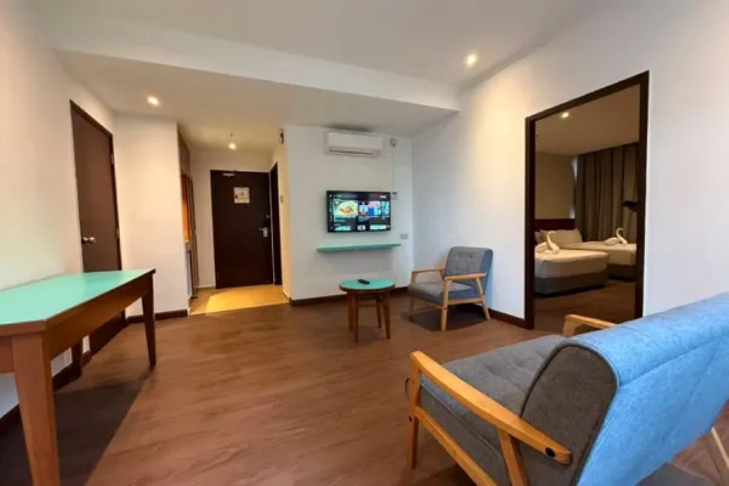 A living room with a sofa, a television mounted on the wall, a small table, and a door leading to another room.