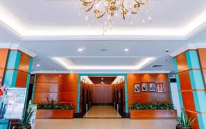 A hotel lobby with a chandelier, a reception desk, and a corridor leading to the rooms.