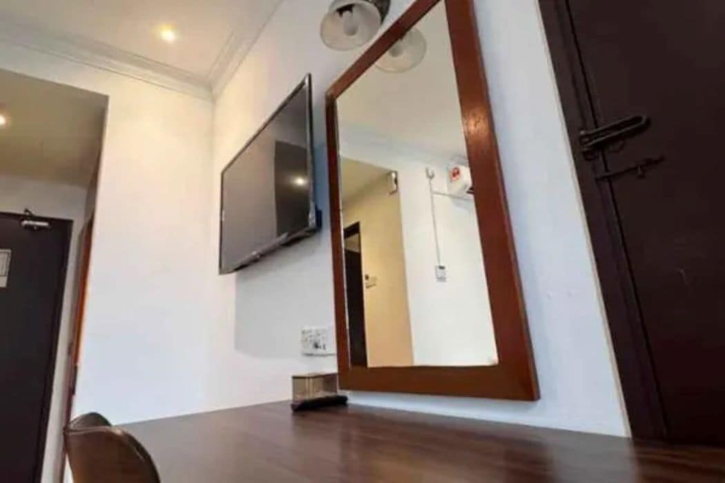 A room with a wooden table, a flat-screen TV mounted on the wall, and a large mirror.