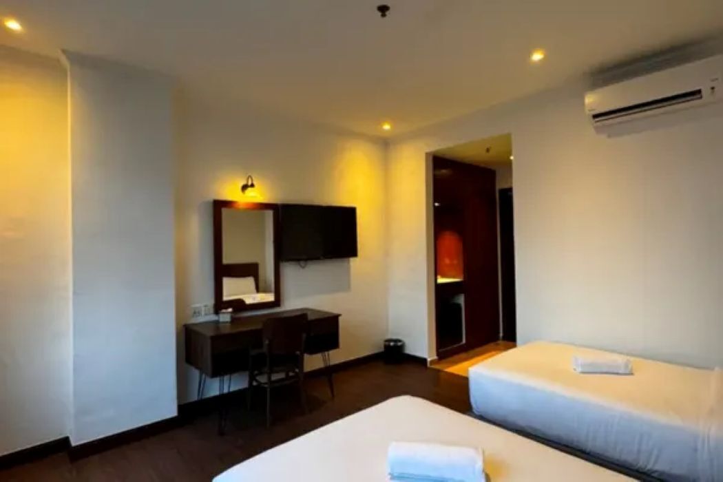 A hotel room with two beds, a desk, a chair, a television, and an air conditioning unit.