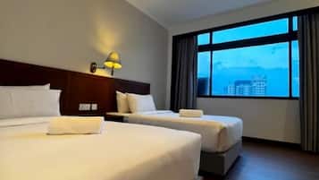 Quarto de hotel com duas camas, uma mesa de cabeceira, abajur e uma grande janela com vista para edifícios.