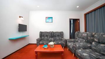 Ein Wohnzimmer mit einer Couch, einem Couchtisch, einem Flachbildfernseher und einem an der Wand montierten Regal.